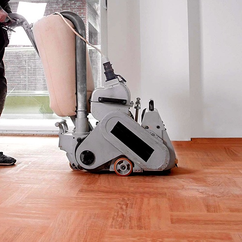 Professional floor sanding machine being pushed on a wooden floor by a worker