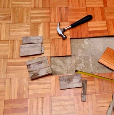 A parquet floor under repair with a hammer and tape measure on top.